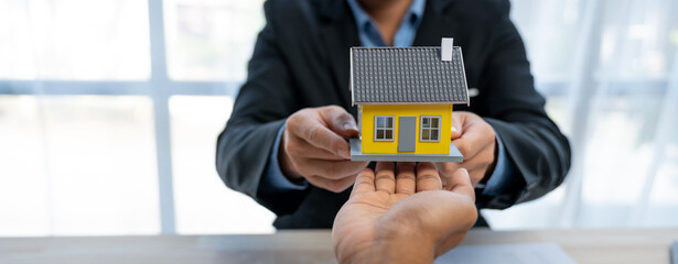 Young Asian real estate agent, and insurance salesman handing over a sample house to a client after signing the sale at the office.