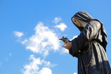 Estátua de Santa Rita de Cássia e céu azul com nuvens ao fundo