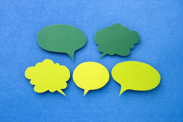 Green speech bubble or text box made of color paper cut on blue paper background.
