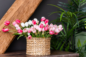 Bright, colorful tulips in a wicker basket on a wooden table