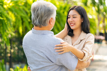 Happy Asian family hanging out together on summer vacation. Attractive adult woman hugging elderly father during shopping at plant shop street market. Father and daughter relationship concept.