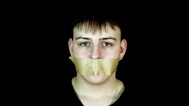 Person Placing Tape Over Mouth of Young Man, Slow Motion. Kidnapping or Free Speech Concept