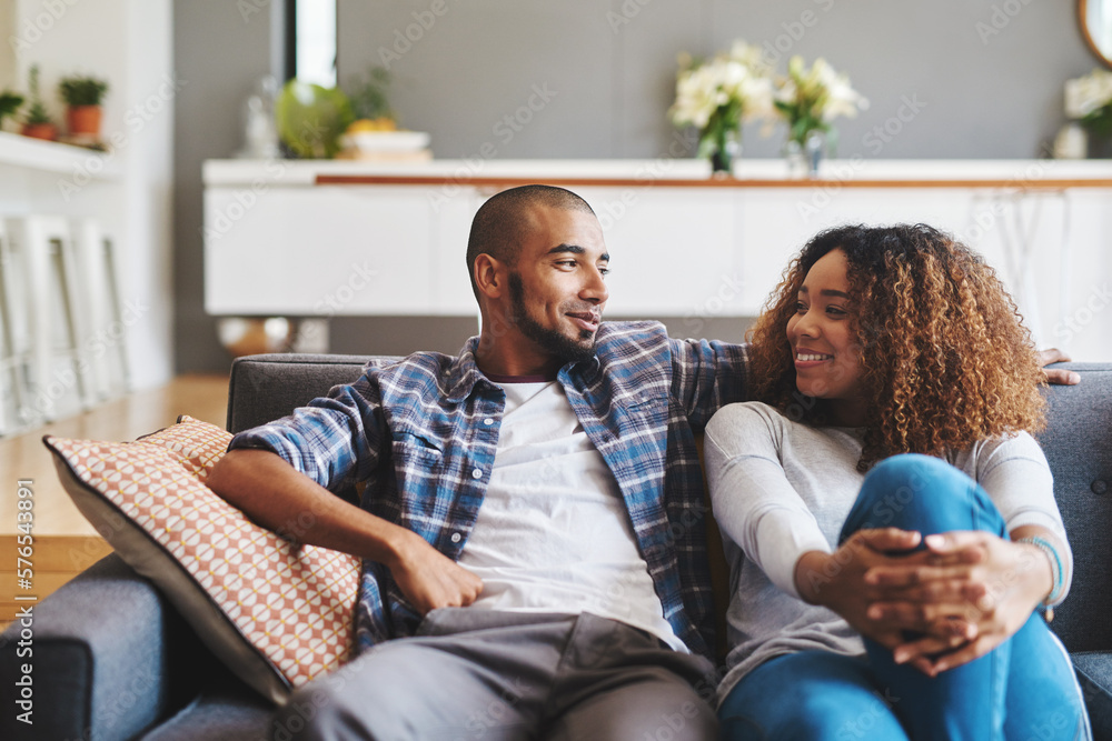 Poster Home is wherever you are. Cropped shot of an affectionate young couple sitting together on their sofa in their living room during the day.