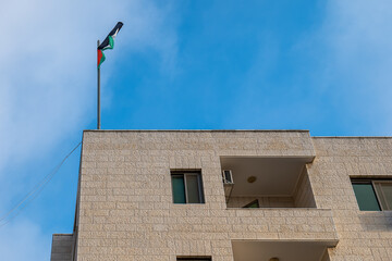 White Stone Brick Building with Palestinian Flag Against Clear Blue Sky