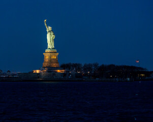 Night Profile of the Statue of Liberty from the Water with US flag in the background