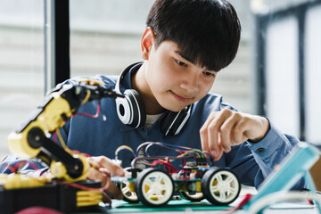 Asian teenager students doing robot arm and robotic cars homework project in house disassemble the circuit and coding. technology of robotics programing and STEM education concept.