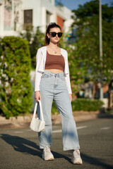 Fototapeta premium Young woman in wide jeans, sunglasses and white cardigan