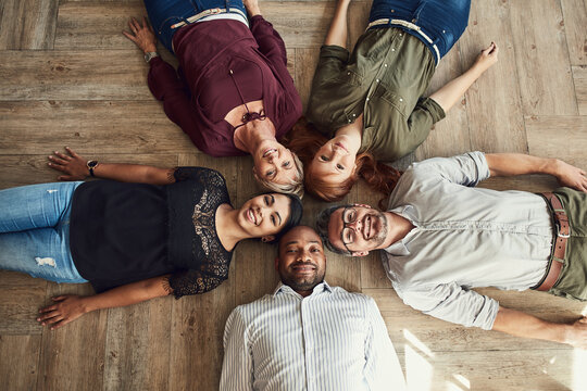 We keep it casual but always professional. High angle portrait of a group of colleagues lying together in a circle on the floor at work.