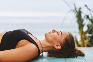 Corpse Pose Young athletic woman in black sport bra doing yoga exercises in front of sea