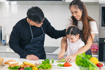 Asian Family people enjoy teaching children cook food using knife for healthy at home