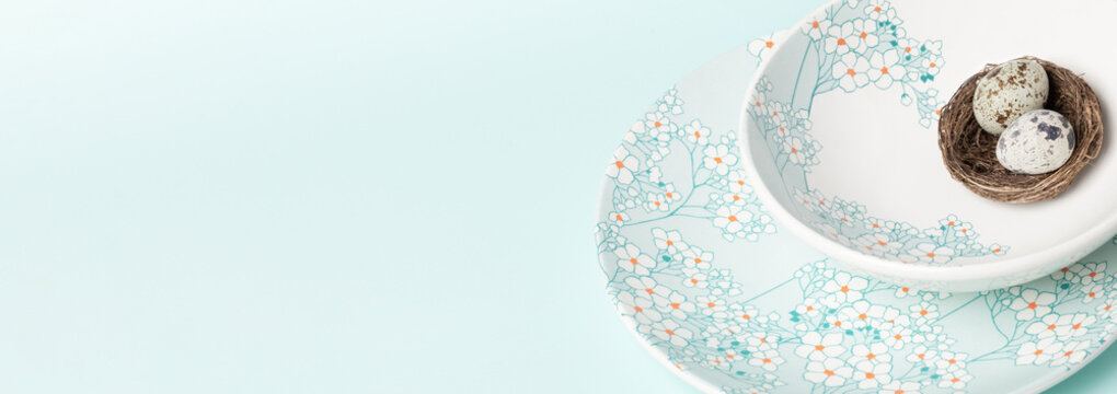 Plates with gentle floral pattern with quail eggs in nest on light blue. Easter banner. Copy space.