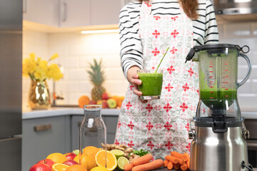 Women making a green healthy vitamin cocktail for detox. Citrus fruits and vegetables in background. Healthy living concept.