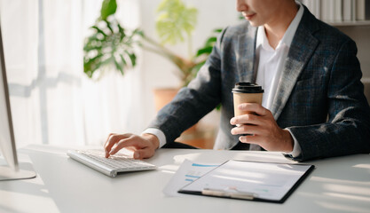 man using laptop and typing on laptop and holding coffee cup in cafe, home office