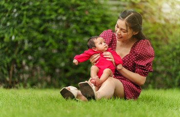 mother holding and playing with her baby newborn while sitting on grass field - Powered by Adobe