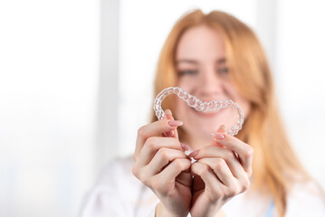 Dental care.Smiling girl with red hair holding heart shaped aligners