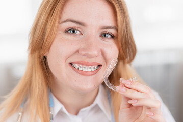 Dental care.Smiling girl with braces on her teeth holds aligners in her hands and shows the difference between them