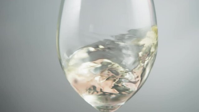 Close up of white wine waving inside a wineglass on a grey background. Slow motion. 