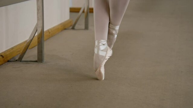 Close-up feet shooting of professional ballerina standing on tiptoe in pointe shoes at dance studio. Ballet dancer prepares for performance. Woman doing classic ballet exercises. Classic ballet school