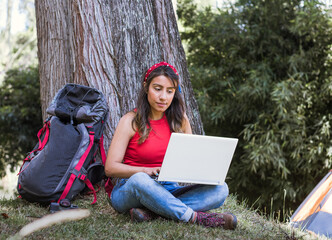 Digital nomad in nature: Latin woman working on laptop under a tree in the woods