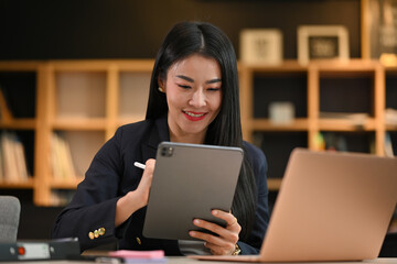 Portrait of charming asian woman manager sitting front of laptop and using digital tablet.