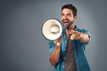 Youre our winner of the day. Studio shot of a handsome young man using a megaphone against a grey background.