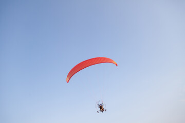 a red motorized paraglider in the blue sky flies with two passengers on a warm summer day. Flying...