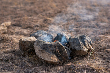 A smoldering bonfire on ground. Make a fire in nature. Stone fire pit in the middle of grass. Camp...