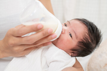 mother feeding baby boy with fresh milk in plastic bottle in bed closeup. mother breastfeeding and...
