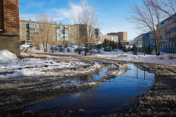 Fototapeta na wymiar One of the city streets. Urban landscape. Spring time. Roadway with large puddles and holes. Slush. Snow melting. Ust-Kamengorsk (kazakhstan)