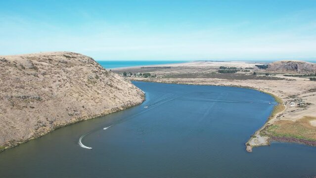 Aerial view of deep-blue lake, coastline, volcanic peninsula and power boats racing around course - Lake Forsyth (New Zealand)