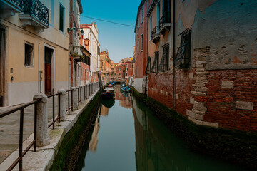 A canal in venice with a red building and a blue sky