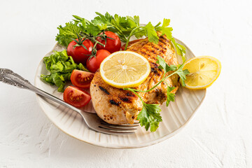large textured ceramic plate with grilled chicken fillet with fresh vegetables. lemon wedges to improve the taste. white background.