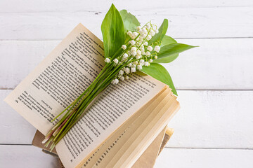 a bouquet of delicate fragrant lilies of the valley lies on an open book and a white wooden table....
