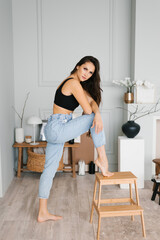 Sensual beautiful young Caucasian woman with long hair in a black top and jeans posing for the camera in the living room