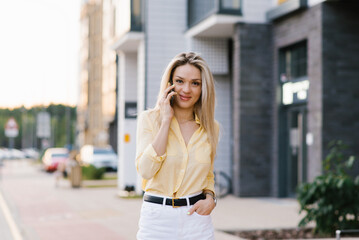 Fototapeta premium Pretty joyful woman is talking on a mobile phone while walking around the city in the summer