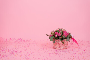 Romantic bouquet of pink roses and eucalyptus in a basket on a pink background with confetti. Birthday gift, Women's Day, Mom's Day, Valentine's Day