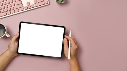 Overhead view of hands holding digital tablet with blank screen over pink background. Top view with copy space for your text