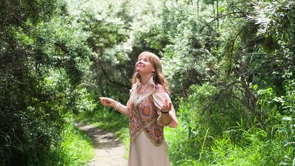 A young woman raises her hands up, the woman is wearing a pink long dress in boho style. A woman is...
