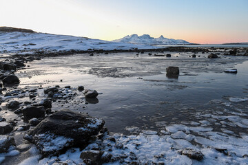 Wide angle shot of ice and boulders along the Norwegian coast, on a snowy winter morning.
