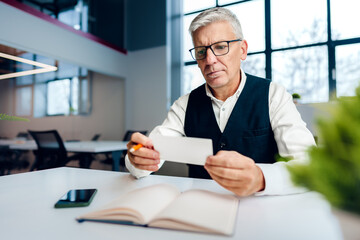 Busy senior man sitting at office desk with papers and making notes