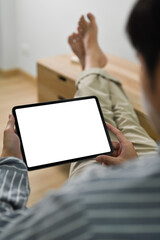Over shoulder man in casual cloth putting legs on table and using digital tablet