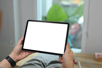 Close up view of hands holding holding digital tablet while sitting in living room. White screen for webpage or advertise text