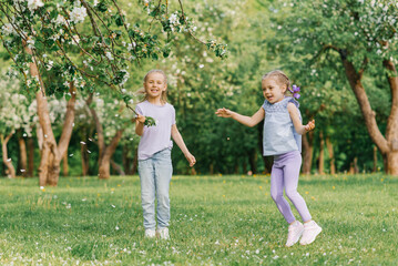 Two little girls, sisters having fun outdoors in a blooming garden