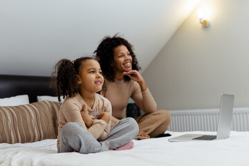 Obraz premium Happy african american woman and her little daughter watching TV