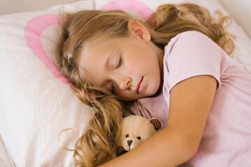 Little girl sleeping with a soft toy in her bed on a pillow is a sweet calm sleep of a child.