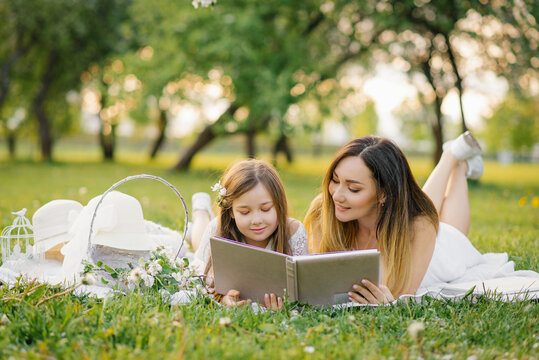 Mom and little daughter are looking at a family album with photos in the summer in the garden. Family values