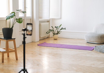 Mobile phone on tripod in empty living room with fitness mats on the floor