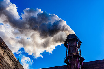 View on smoke pipe of the factory against blue sky. Environmental pollution