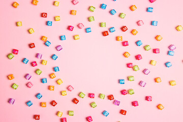 Round frame from colorful letter beads on pink background. Flat lay, copy space.