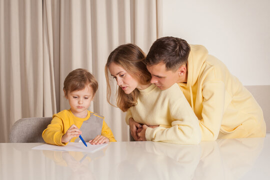 Mom and dad in yellow clothes with their child son sitting by the table and drawing
